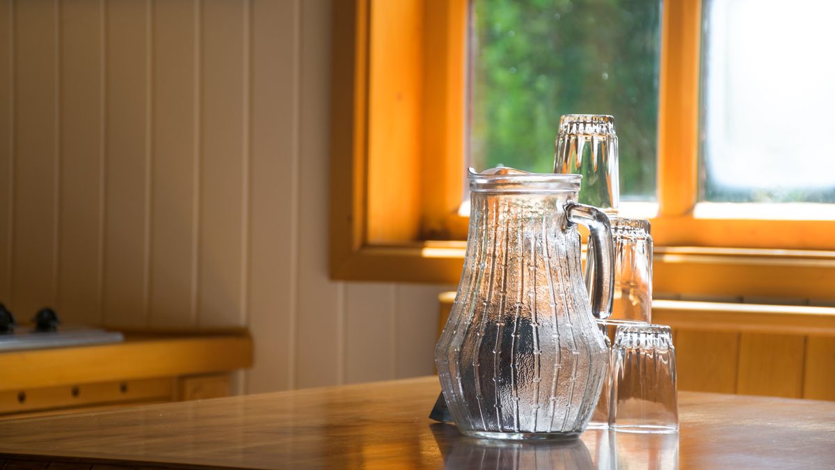 A glass jug and glasses on a kitchen table in morning light from a window
